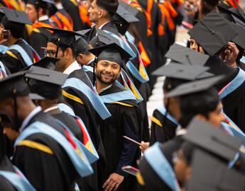In a lineup of graduates, one man turns his back and smiles in the direction of the camera