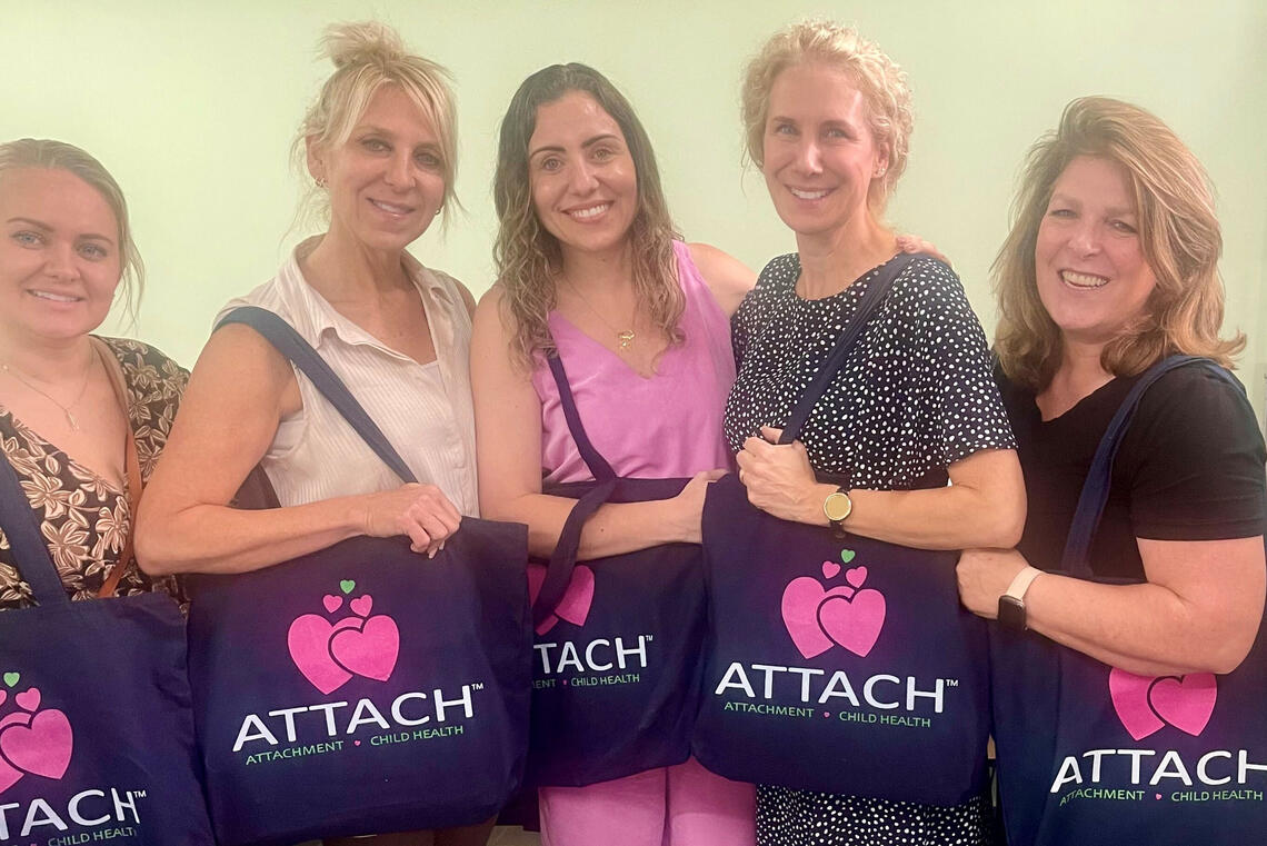 A group of women stand holding tote bags that say ATTACH on them